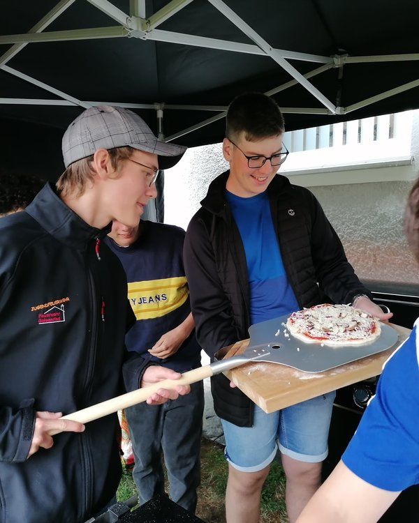 Zwei Jungen, die mit einem Pizzaschieber eine rohe Pizza von einem Brettchen aufnehmen | © RÖSLE GROUP