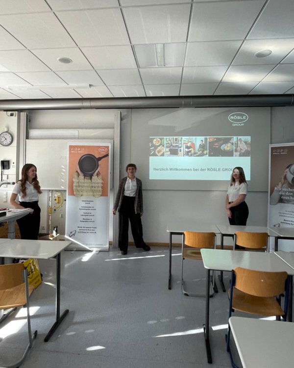 Drei Frauen stehen in einem Klassenzimmer vor einem RÖSLE Banner und einer RÖSLE Präsentation | © RÖSLE GROUP