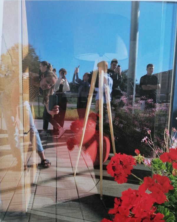 Ein Foto liegt auf einem Tisch, darauf ist die Reflektion von roten Blumen und fotografierenden Jugendlichen in einer Scheibe zu sehen | © RÖSLE GROUP
