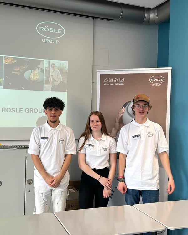 Berufsorientierungstag Realschule 2024 | © RÖSLE GROUP Zwei Jungen und ein Mädchen, die in einem Klassenzimmer vor einem RÖSLE GROUP Banner und einer Präsentation stehen | © RÖSLE GROUP