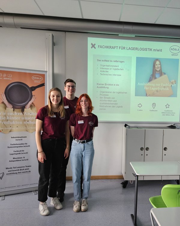 Drei Azubis stehen in einem Klassenzimmer vor einer Leinwand mit einer Präsentation zwischen zwei RÖSLE GROUP Bannern | © RÖSLE GROUP