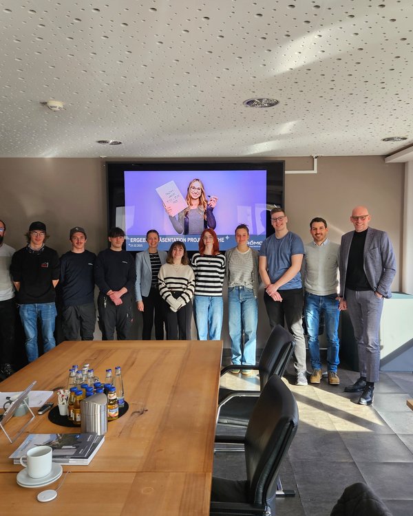 Projektwoche 2025 | © RÖSLE GROUP Die Azubis der RÖSLE GROUP stehen mit einer Frau und drei Männern vor einem großen Bildschirm in einem Besprechungsraum und schauen lachend zur Kamera | © RÖSLE GROUP