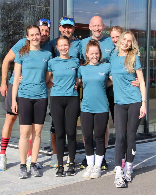 Laufgruppe 2025 | © RÖSLE GROUP Eine Personengruppe in einheitlich blauen RÖSLE-Trikots steht Arm in Arm vor dem RÖSLE Shop und lacht in die Kamera | © RÖSLE GROUP