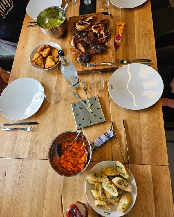 Azubi-Kochen Planspiel 2025 | © RÖSLE GROUP Gedeckter Tisch, auf dem Gurken- und Karottensalat, Kräuter-Baguette, Kartoffelecken und Steak stehen | © RÖSLE GROUP