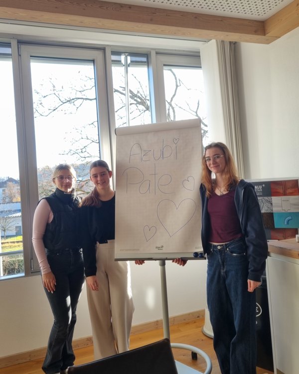 3 Mädchen stehen  neben einem Schild auf dem "Azubi Pate" steht. Sie lächeln alle in die Kamera | © RÖSLE GROUP